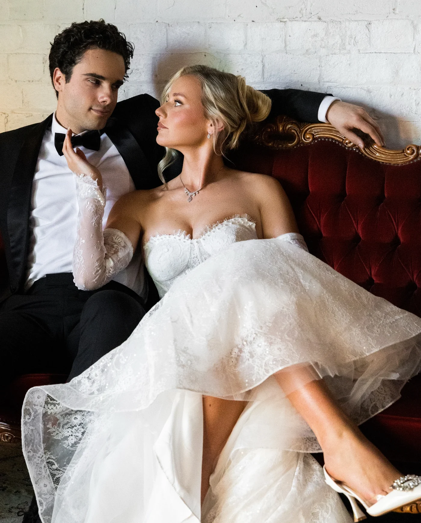 Bride and groom together on a red velvet sofa.